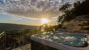 Un bain à remous sur un balcon offrant une vue imprenable sur le coucher de soleil et les montagnes.