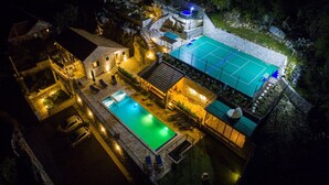 Vue aérienne d’une propriété dotée d’une piscine, d’un court de tennis et de bâtiments en pierre.