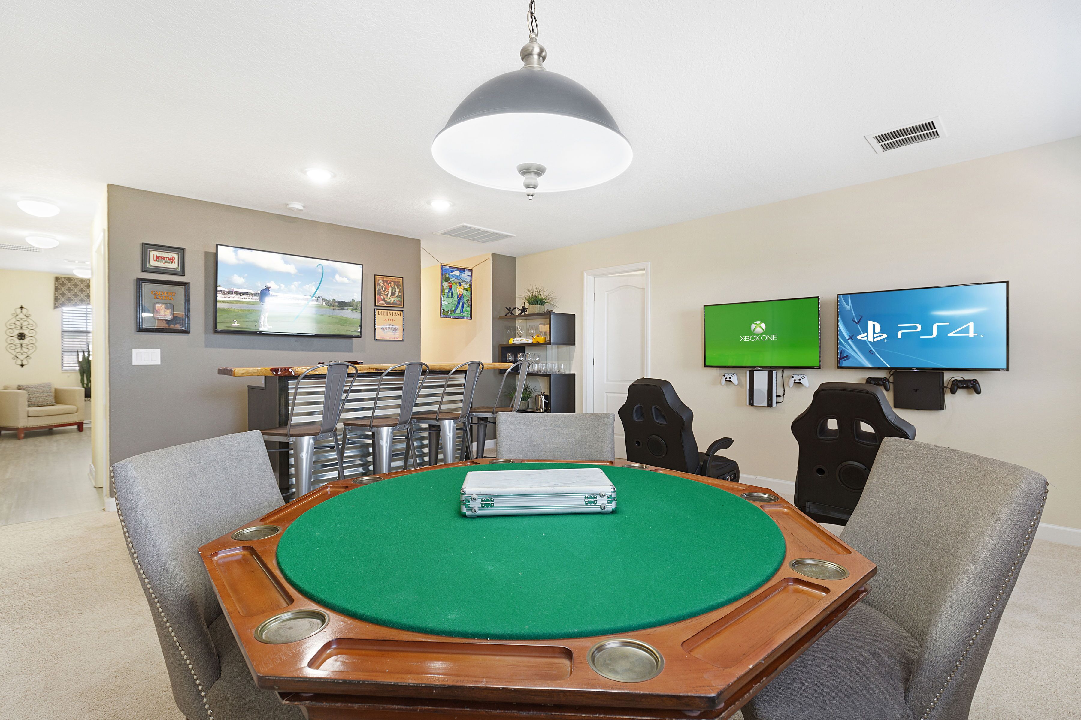Ett rum med ett biljardbord, spelstolar, en tv-skärm som visar logotyperna för Xbox och PS4 samt en taklampa.