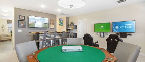 Ett rum med ett biljardbord, spelstolar, en tv-skärm som visar logotyperna för Xbox och PS4 samt en taklampa.