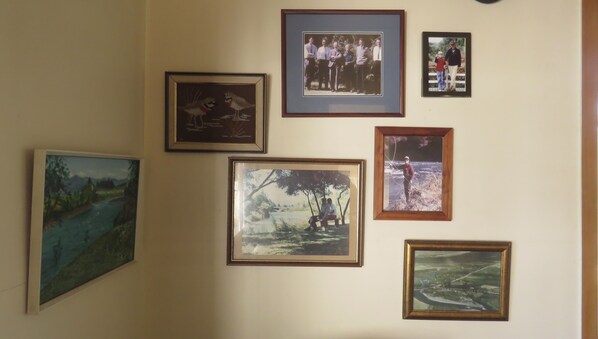 A wall with various framed pictures, including landscapes and a group photo. - Tongariro Riverside holiday house (Turangi)