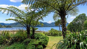 Un exuberante jardín con helechos y palmeras, un camino y una vista a la playa y las montañas a lo lejos.