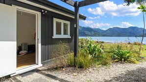 Una casa moderna con terraza de madera, una puerta que da a una habitación y vistas a montañas y un lago.