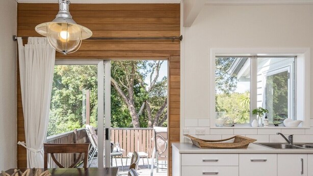 Una cucina moderna con mobili bianchi, un'area pranzo con tavolo e sedie in legno, e vista sull'esterno tramite una porta scorrevole in vetro.
