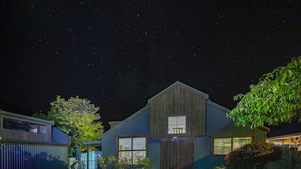 Una casa moderna con un garage, un piccolo portico e un albero nel giardino.