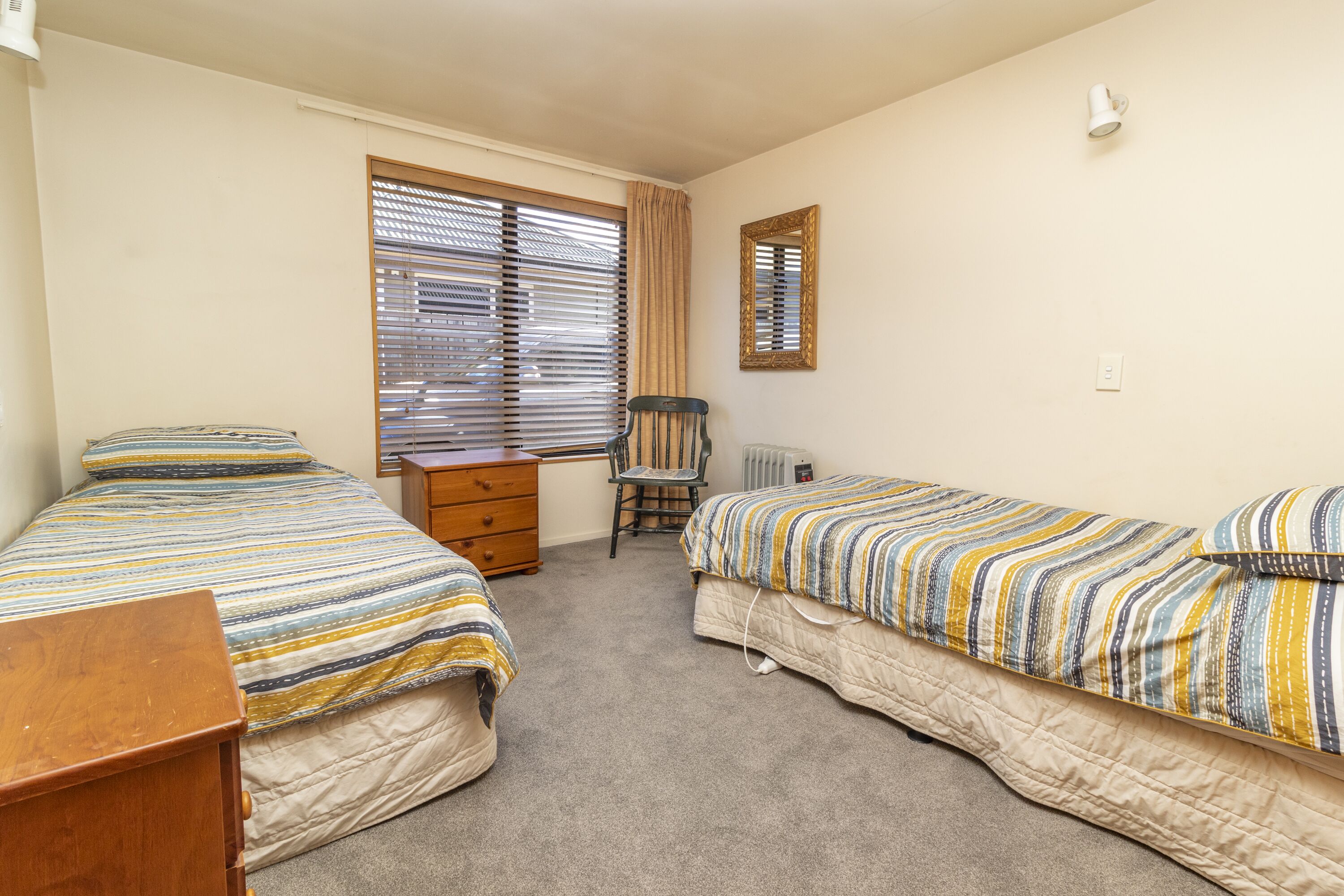 A bedroom with two beds, a chair, a dresser, and a window with blinds.