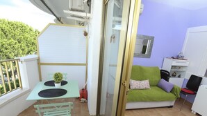 Un balcon avec une table, des chaises, une petite plante en pot et un canapé vert agrémenté de coussins.