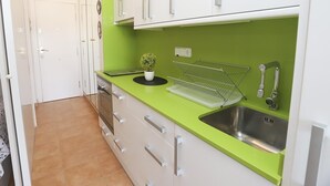 Une cuisine moderne avec des meubles blancs, un plan de travail vert, un évier en acier inoxydable et une petite plante en pot.