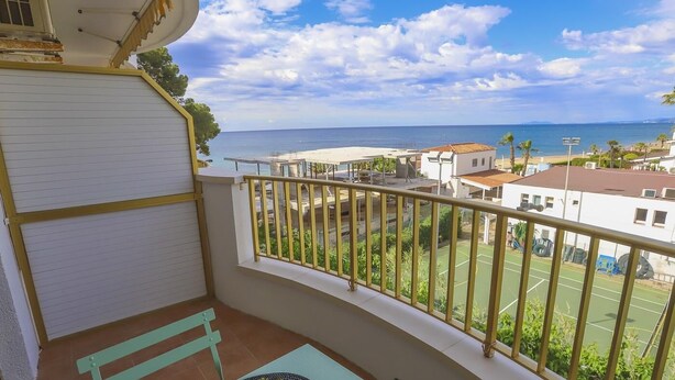 Un balcon avec vue sur la mer, un court de tennis et un bâtiment avec un toit rouge.
