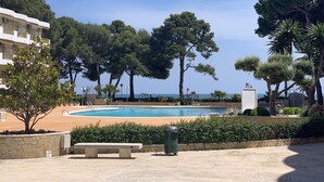 Un espace piscine offrant une vue dégagée sur la mer, entouré d’arbres et d’un bâtiment.