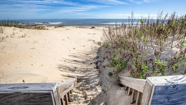 Ein Sandstrand mit Holzbanken und freiem Blick auf das Meer.