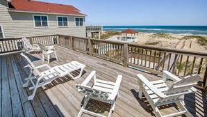 Eine Holzterrasse mit weißen Liegestühlen mit Blick auf einen Strand.