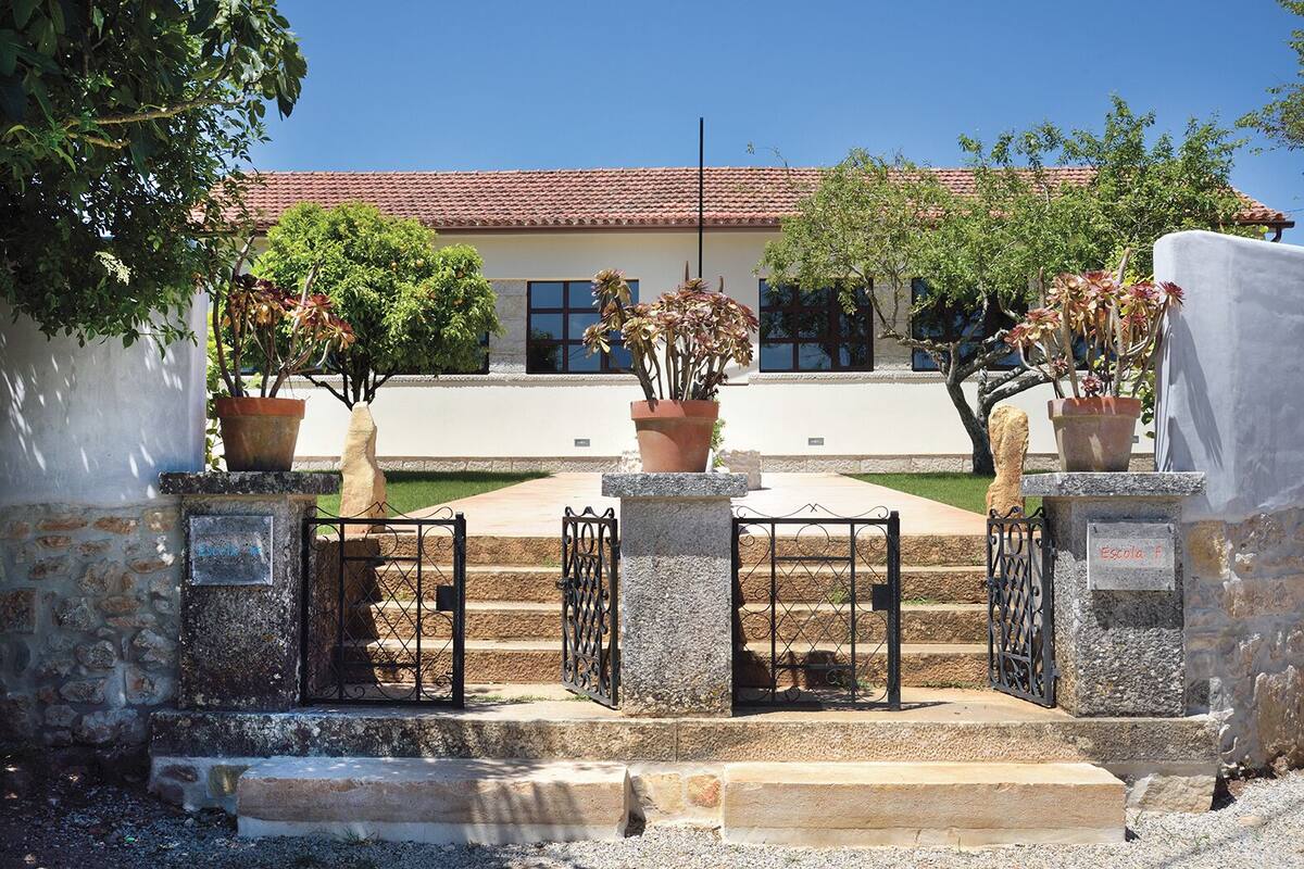 A stone staircase leading to a building with a tiled roof, surrounded by potted plants and a metal gate.