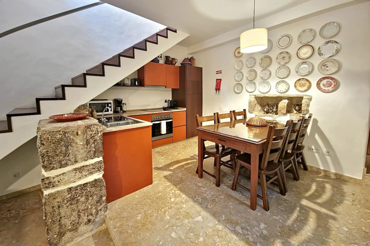 A modern kitchen with a central island, a dining area with a table and chairs, and a staircase with a unique design.