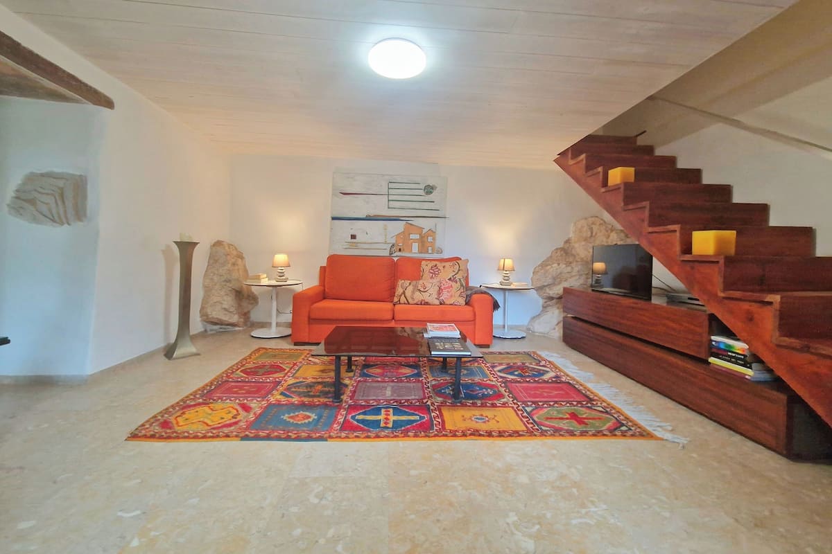 A living room with a wooden staircase, a colorful rug, a sofa, and a painting on the wall.