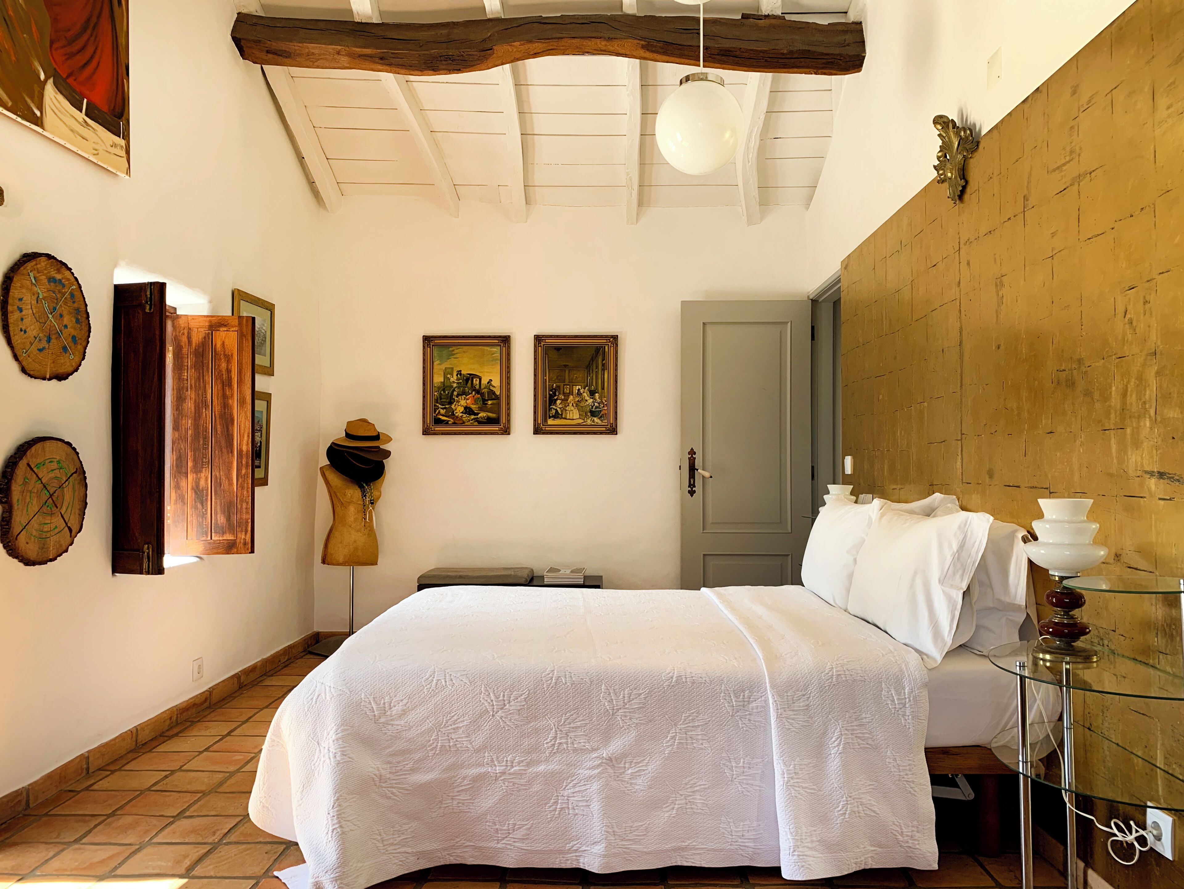 A bedroom with a bed, wooden ceiling beams, a door, and two framed paintings on the wall.