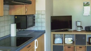 Una cocina con microondas, televisor de pantalla plana, cafetera y tostadora sobre un estante de madera.