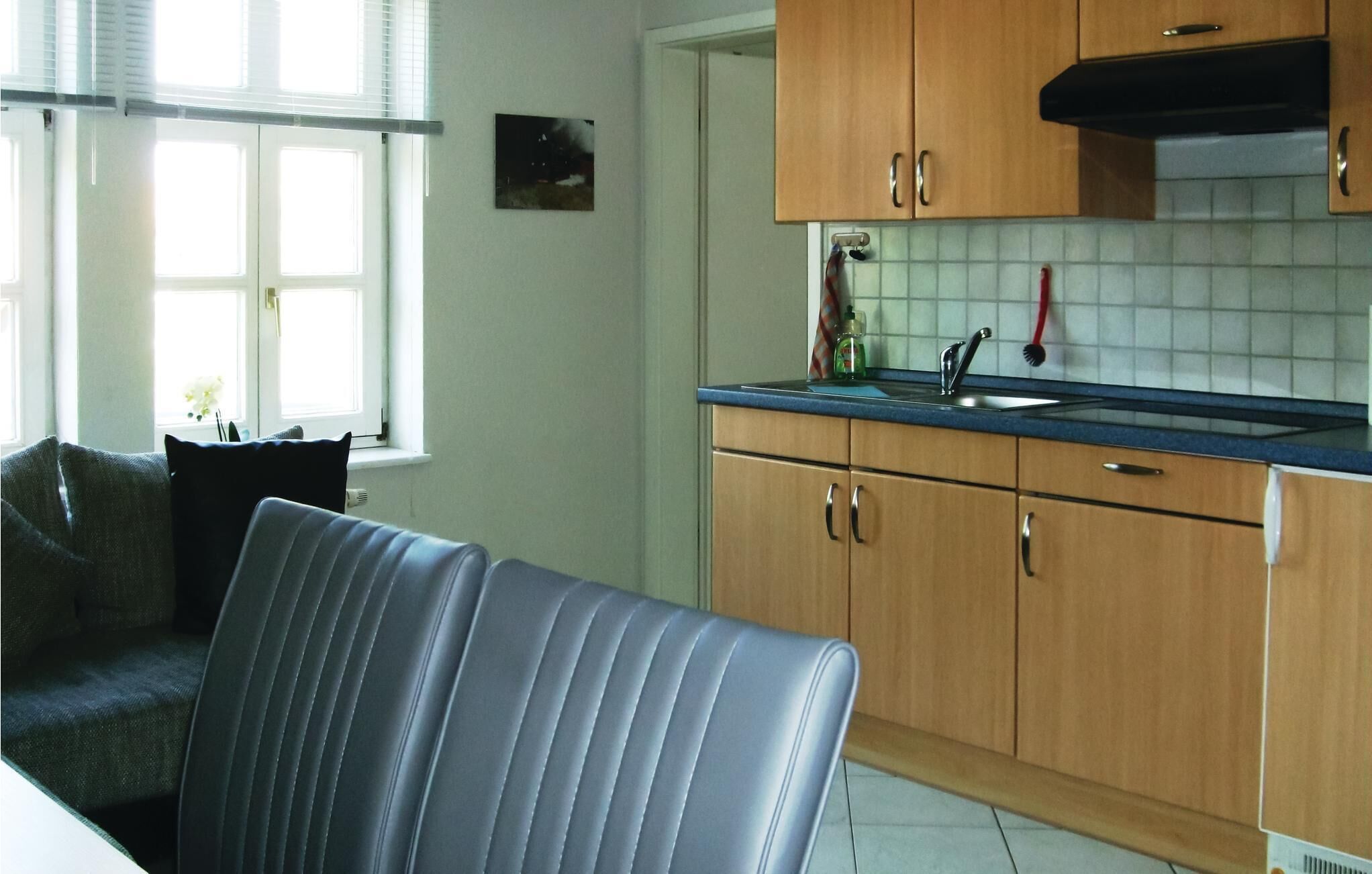 Een moderne keuken met houten kastjes, een blauw aanrecht en een raam met witte luxaflex.