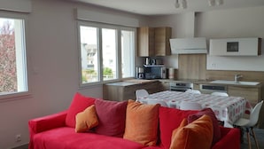 Ein modernes Wohnzimmer mit einem roten Sofa, einem Esstisch mit Stühlen und einer Küchenzeile mit Schränken und einer Mikrowelle.