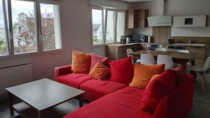 Eine moderne Küche mit Essbereich, ein rotes Sofa mit orangefarbenen Kissen und großen Fenstern.