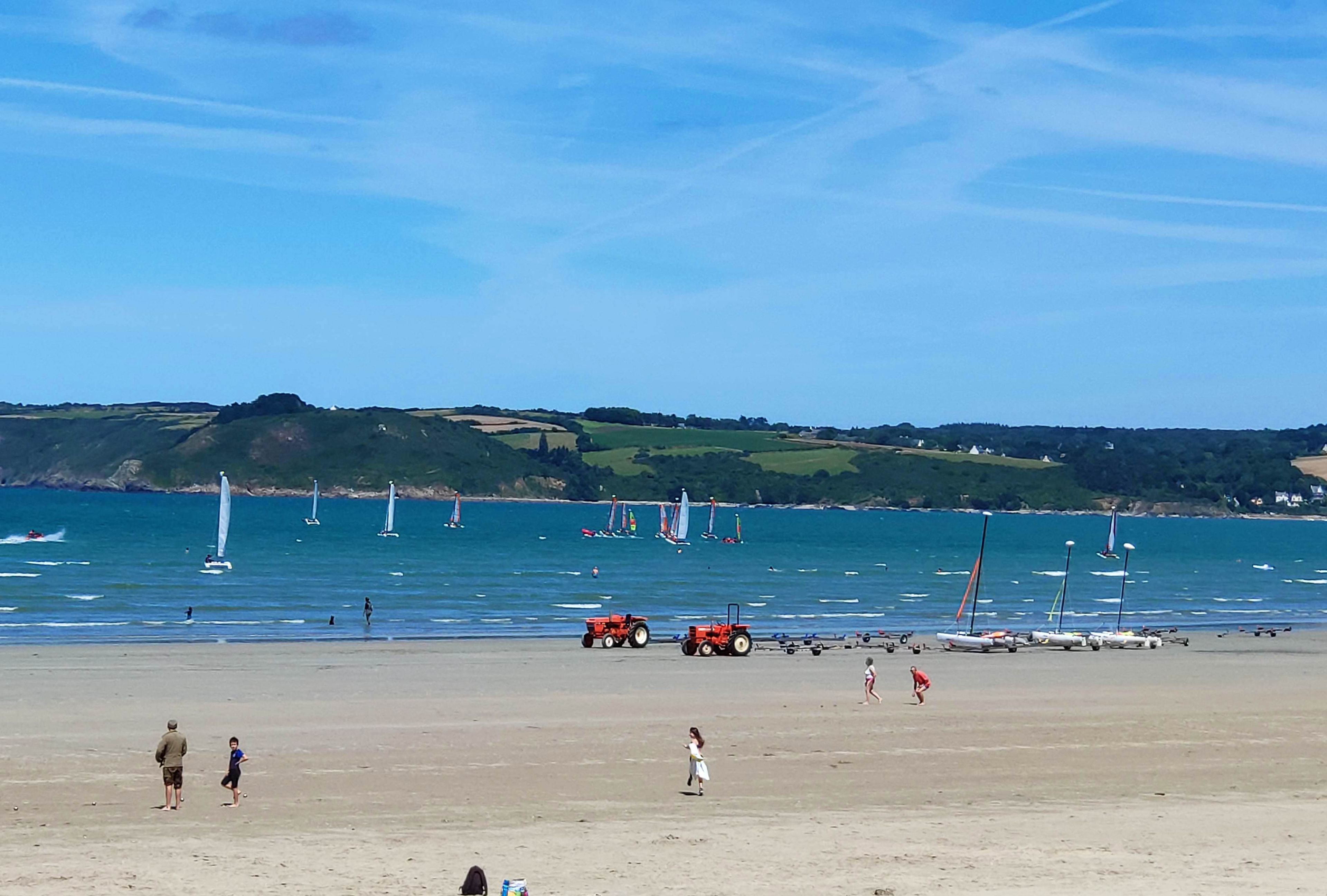 A beach with sailboats, a tractor, and people.