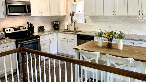 A modern kitchen with white cabinets, stainless steel appliances, and a wooden dining table with chairs.