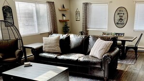 A living room with a leather sofa, a wooden coffee table, and a dining table with chairs.