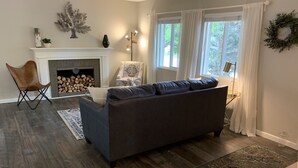 A living room with a fireplace, a sofa, a chair, and a window with curtains.