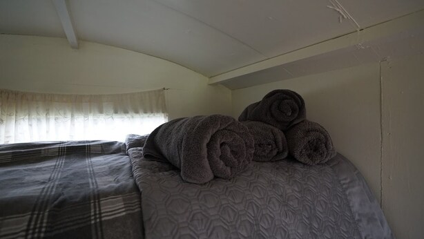 A single bed with a patterned blanket and rolled towels. - Shepherd's Hut @ Westcote (Hawick)