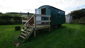 Une maison mobile verte, dotée d’une terrasse en bois et d’un escalier menant à une mezzanine aménagée en espace nuit.