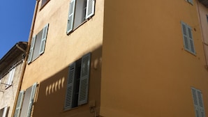 Ein mehrgeschossiges Gebäude mit gelber Fassade, zahlreichen Fenstern mit Fensterläden und einer sichtbaren Stromleitung.