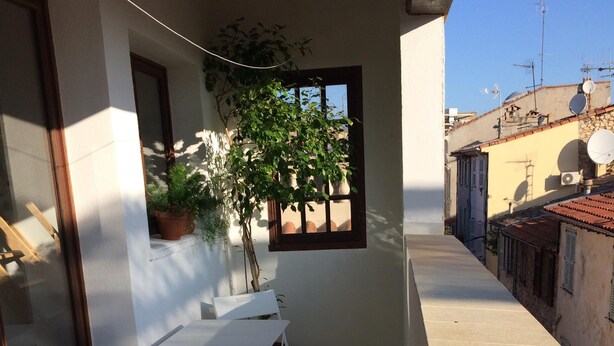 Ein Balkon mit Tisch und Stühlen, einem Blumentopf und Blick auf benachbarte Gebäude.