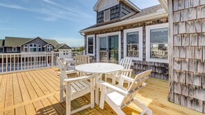 Um deck de madeira com uma mesa redonda e cadeiras, uma área coberta com janelas e vista para outros edifícios.