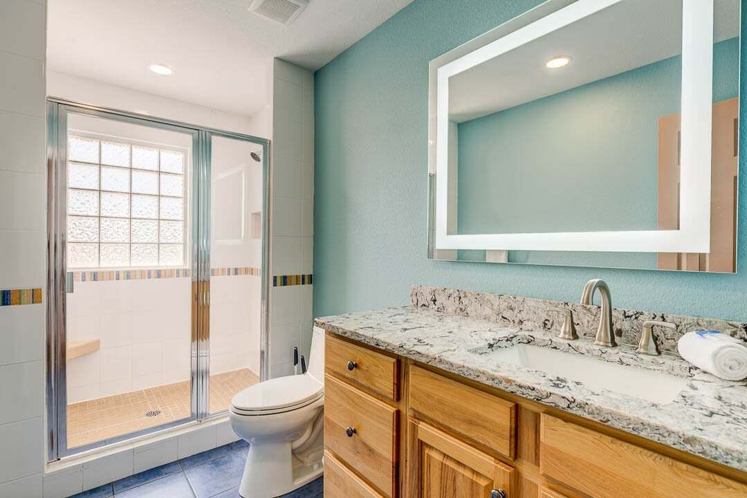 Een badkamer met een douchecabine van glas, een toilet, een wastafel met een marmeren aanrechtblad, houten kastjes en een grote spiegel.