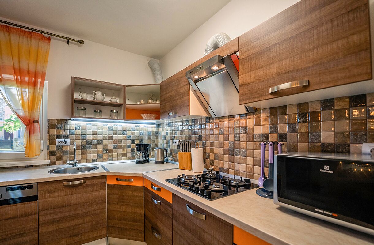 Una cocina moderna con armarios de madera, estufa a gas, microondas y un ventanal con cortinas.