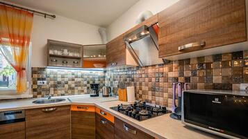 Una cocina moderna con armarios de madera, estufa a gas, microondas y un ventanal con cortinas.