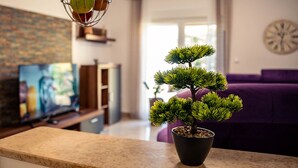 Un salon avec un arbre bonsai en pot, un téléviseur et un canapé violet.