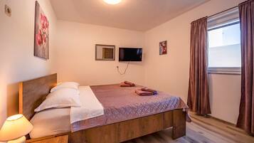A bedroom with a wooden bed, a flat-screen TV, a window with curtains, and a painting on the wall.