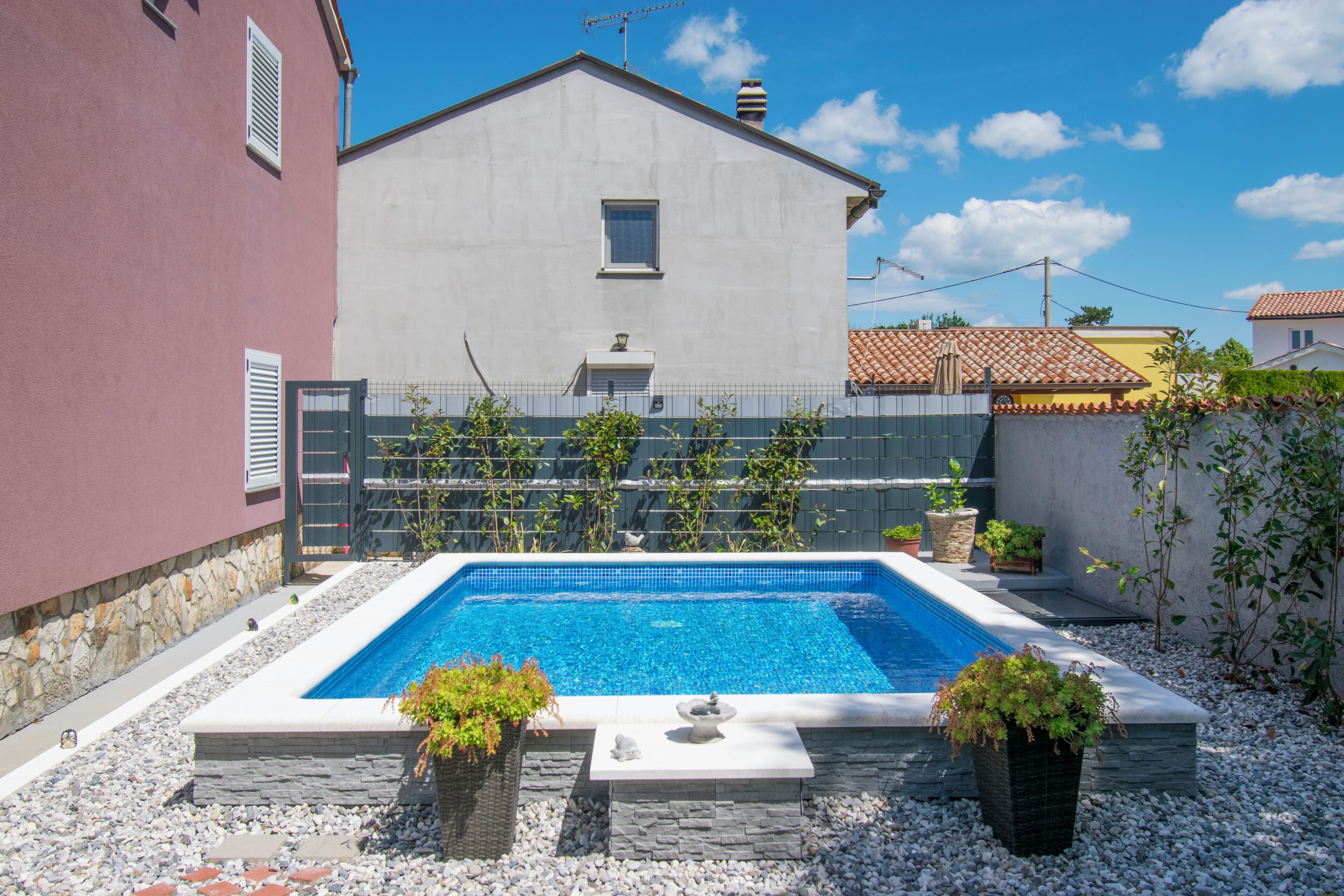 A swimming pool with a stone border, surrounded by pebbles and potted plants.