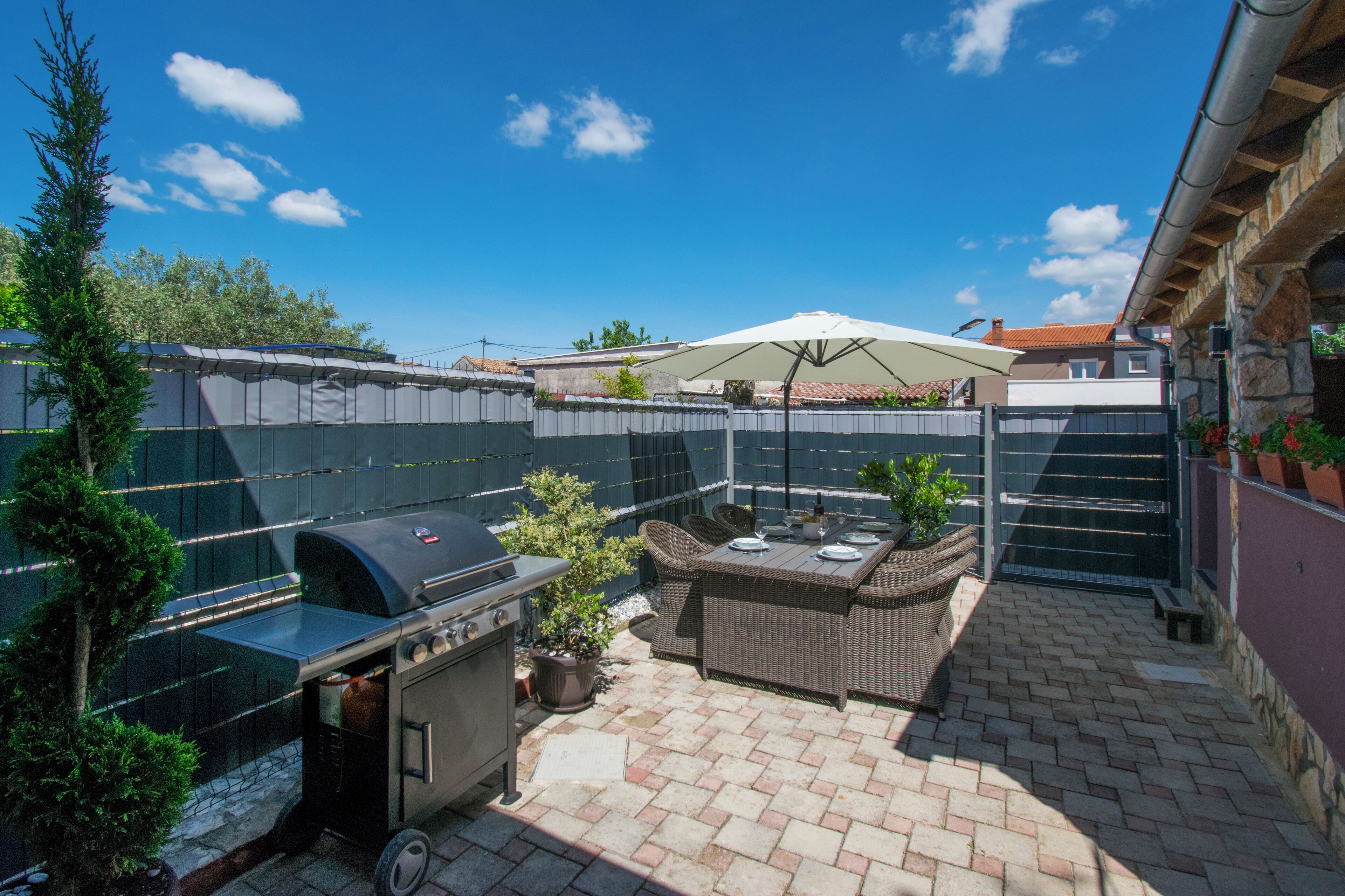 A patio area with a grill, wicker furniture, and a large umbrella.