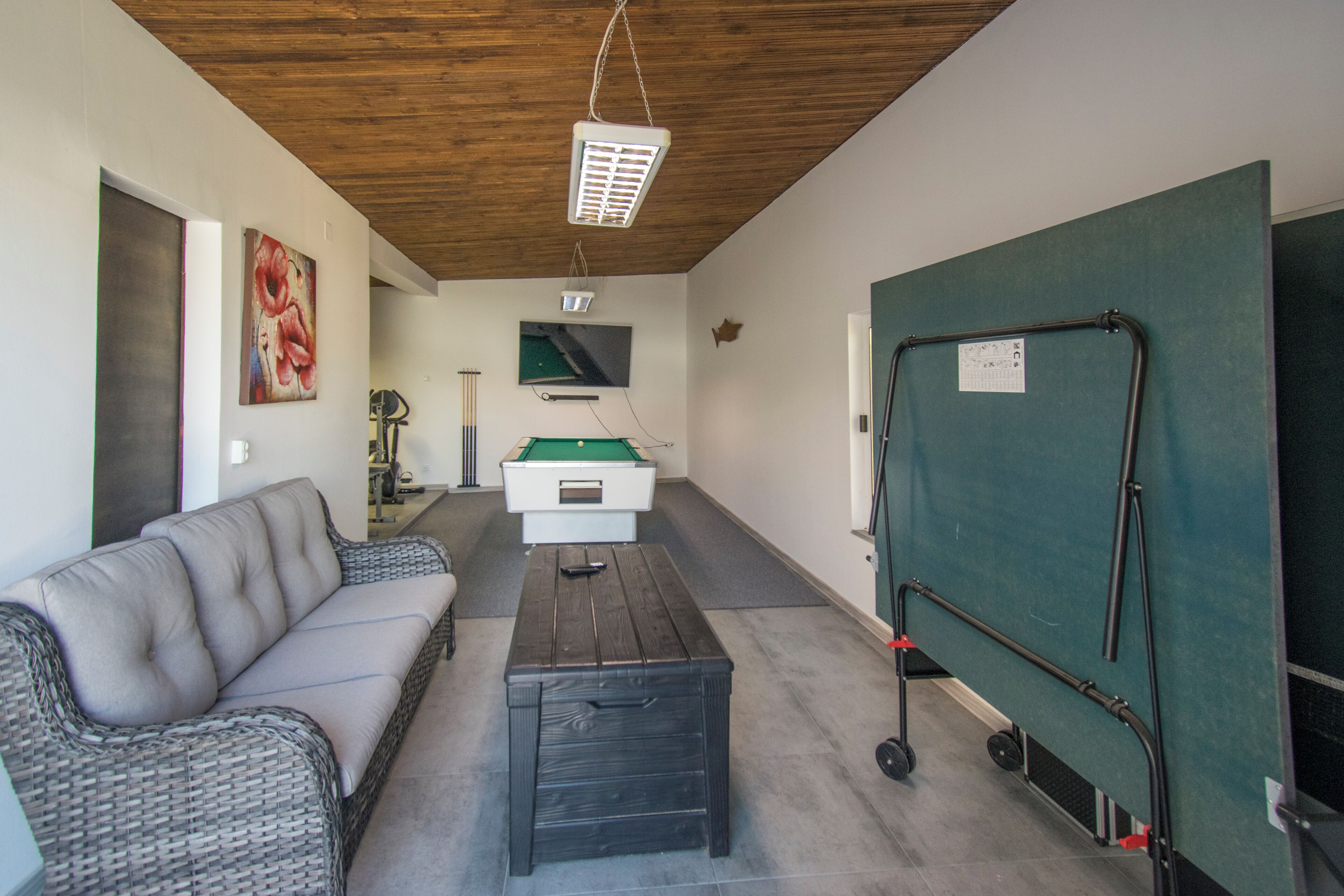Een kamer met een bank, een pooltafel, een biljarthouder en een groene scheidingswand.
