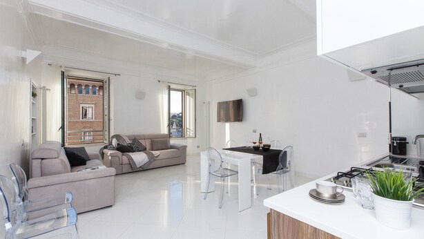 A modern living room with a sofa, a dining table, and chairs. There is a kitchen area with a stove and a sink. - Rental In Rome Piazza Venezia View Luxury Apartments (Rome)