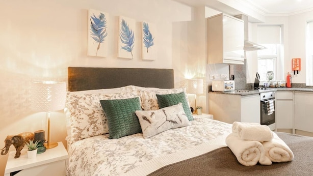 Quarto moderno com uma cama grande, uma mesa de cabeceira, uma luminária e vista para a cozinha.