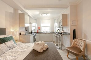 Una habitación de hotel moderna con cama, zona de estar con una silla, cocina y baño.
