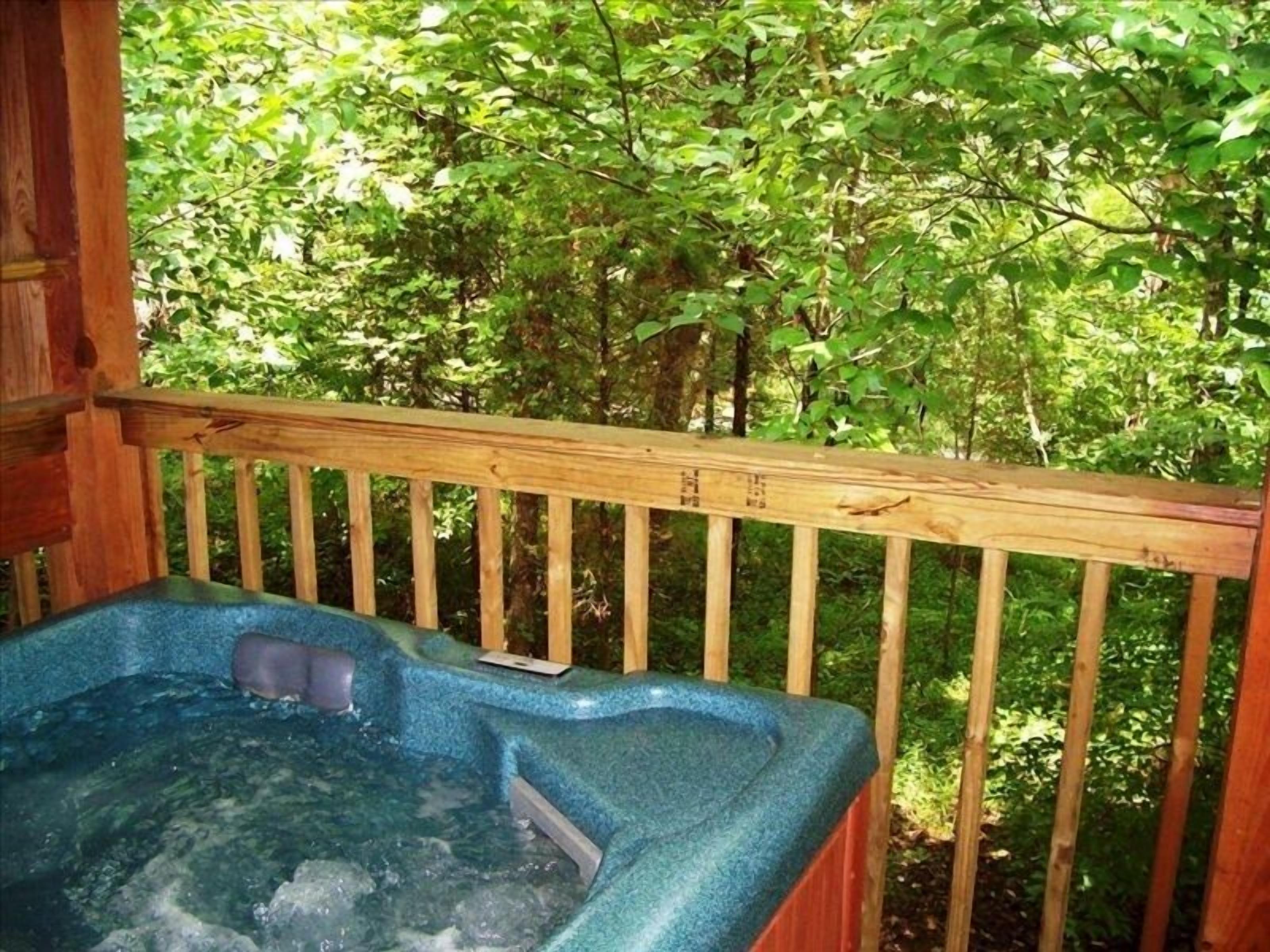 Ein Whirlpool mit einer Holzterrasse und Blick auf ein bewaldetes Gebiet.