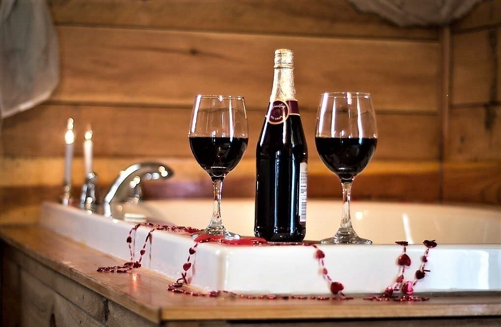L’intérieur d’un chalet en bois, avec un évier, deux verres de vin rouge et une bouteille de vin.