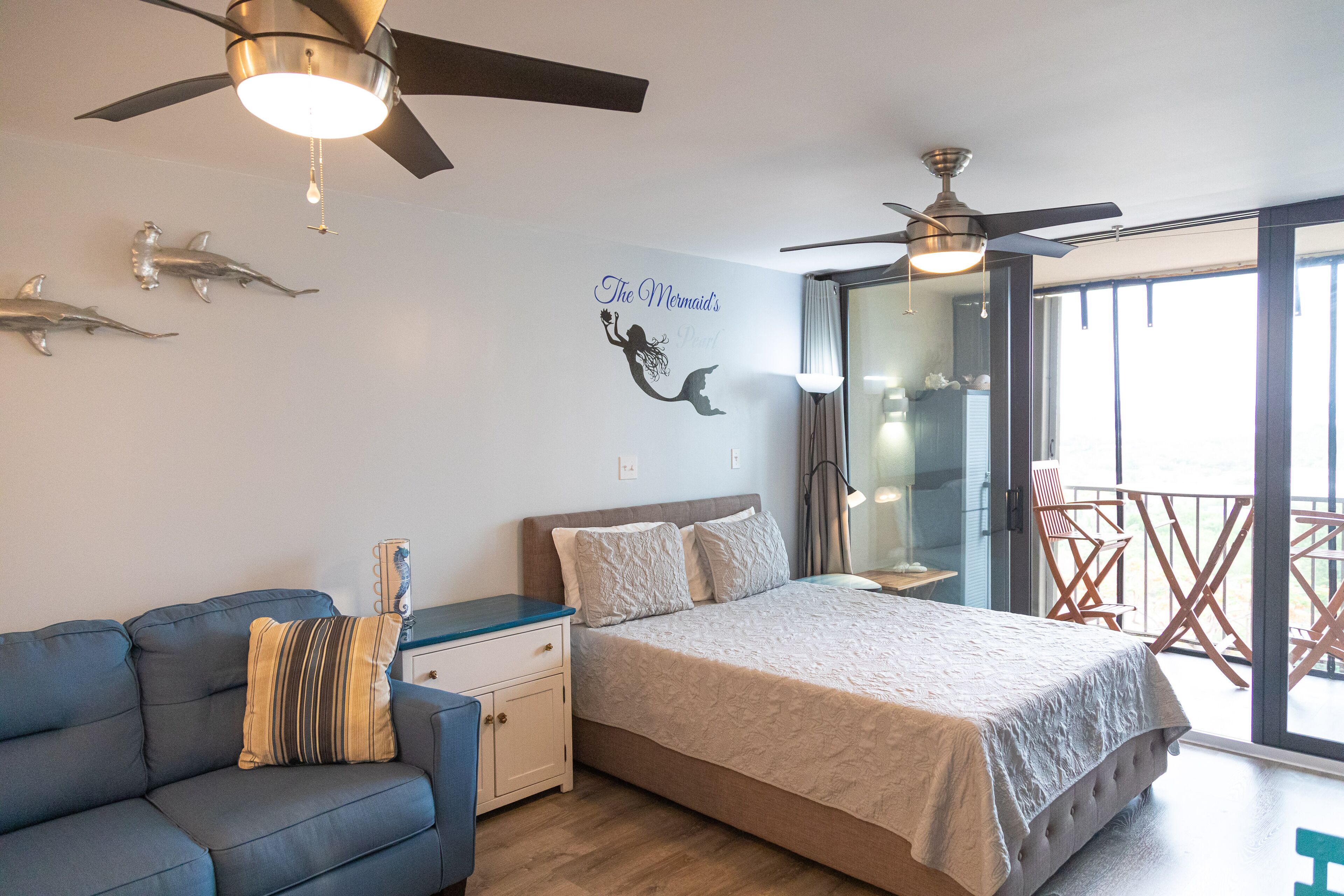 Un dormitorio con cama, sofá, ventilador de techo y balcón con una silla.