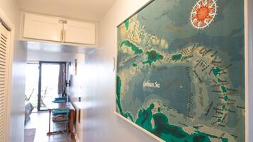 A hallway with a large map of the Caribbean Sea on the wall, a dining area with a table and chairs, and a kitchen area with cabinets and a refrigerator.