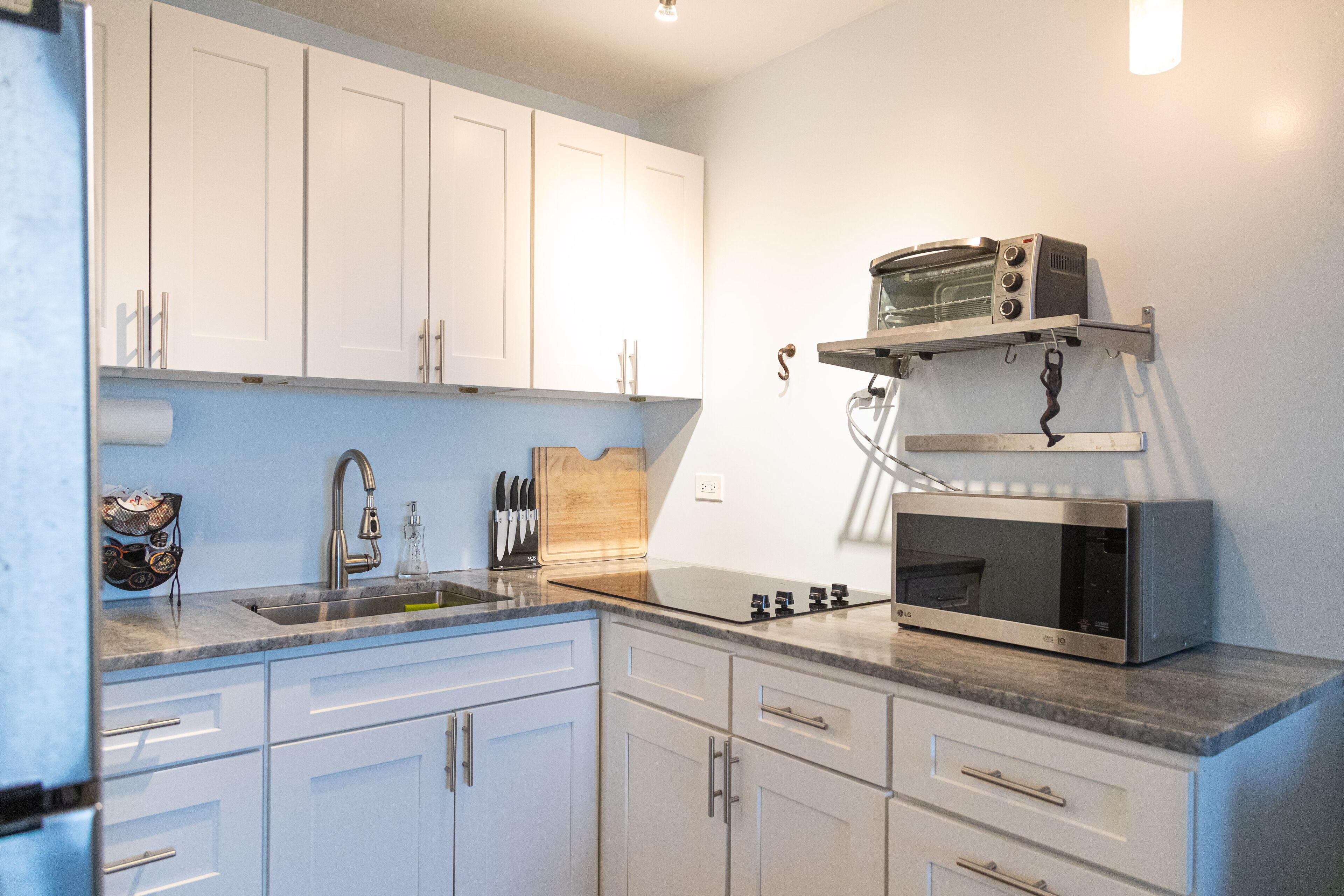 A kitchen with white cabinets, a stainless steel sink, a microwave, and a toaster on a countertop.