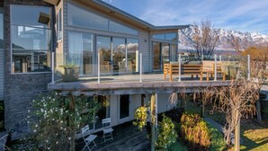 Een modern huis met een ruim terras, glazen wanden en uitzicht op bergen.